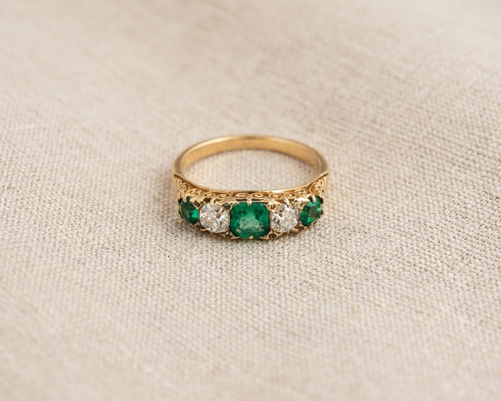 Emerald and diamond anniversary ring featuring an alternating row of three green emeralds and two old-cut diamonds in yellow gold, antique-inspired jewelry for women, green gemstone five-stone band.
