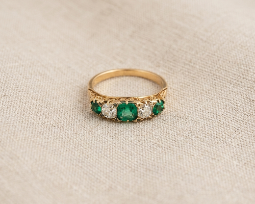 Emerald and diamond anniversary ring featuring an alternating row of three green emeralds and two old-cut diamonds in yellow gold, antique-inspired jewelry for women, green gemstone five-stone band.