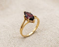 An exquisite 9ct yellow gold ring featuring a deep crimson marquise-cut garnet in a secure prong setting, resting on a textured light beige linen fabric surface under professional studio lighting.