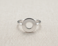 A highly polished sterling silver geometric ring with a prominent, flat circular face and a precise central hole, resting centered on a textured, light-oatmeal linen background.