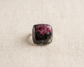 Front view of a sterling silver statement ring featuring a cushion-shaped eudialyte cabochon gemstone with natural magenta pink and black patterns in a polished bezel setting.
