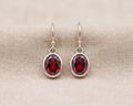 A pair of brilliant-cut, round, deep-red garnet earrings set in a simple sterling silver bezel with elegant fishhook ear wires.