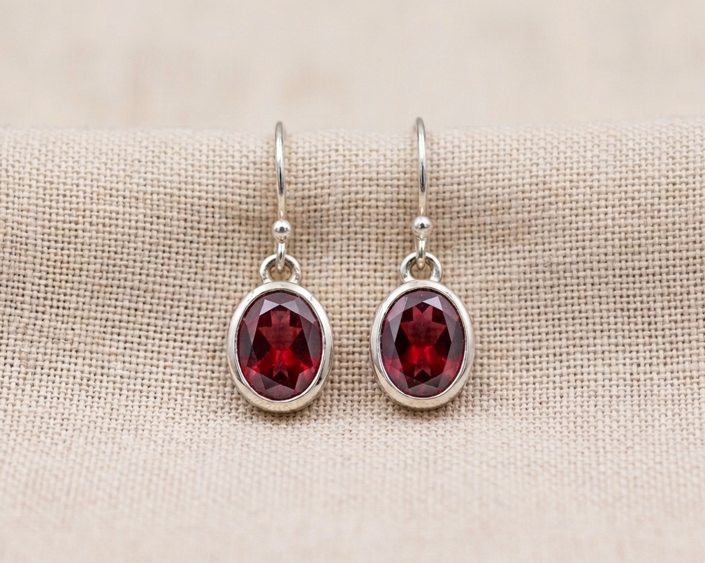 A pair of brilliant-cut, round, deep-red garnet earrings set in a simple sterling silver bezel with elegant fishhook ear wires.