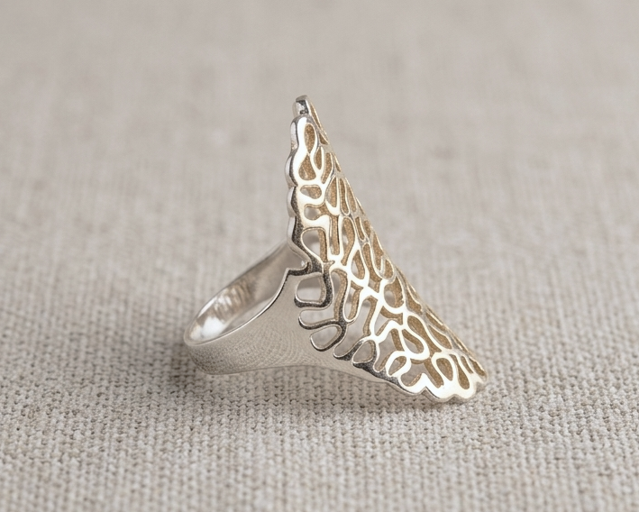 A handcrafted 925 sterling silver statement ring featuring an intricate organic filigree cutout design, shown standing in a top-down view on a light oatmeal-colored linen background under professional studio lighting. Side view.