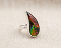 Sterling silver ring with a large, polished teardrop-shaped natural ammolite gemstone, displaying an iridescent play of red, green, and gold colours on a dark matrix.