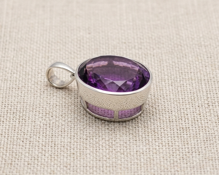 Side-profile studio photograph of an oval-shaped, faceted natural purple amethyst gemstone bezel-set in polished sterling silver. The pendant features a smooth, substantial silver bail.