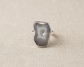 Irregular natural organic grey and white Seafoam Agate slice ring with a round bezel-set blue topaz center stone, all set in sterling silver, displayed on a light linen fabric.