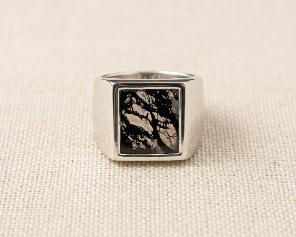 Polished sterling silver Scribe-style signet ring with a natural, unique moss agate stone panel featuring dark green dendritic inclusions, displayed on a light linen fabric. 
