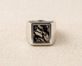 Polished sterling silver Scribe-style signet ring with a natural, unique moss agate stone panel featuring dark green dendritic inclusions, displayed on a light linen fabric. 