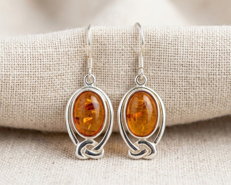 A matched pair of oval genuine Baltic Amber drop earrings set in detailed .925 sterling silver Celtic knotwork settings, featuring comfortable hooks for pierced ears.