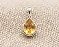 Professional photo of a polished sterling silver pendant featuring a vibrant pear-cut citrine gemstone, resting on a textured linen surface with soft studio lighting.