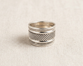 Substantial sterling silver wide band ring featuring an intricate oxidized diagonal woven pattern bordered by delicate rope-twist edges, displayed on a textured light linen background.