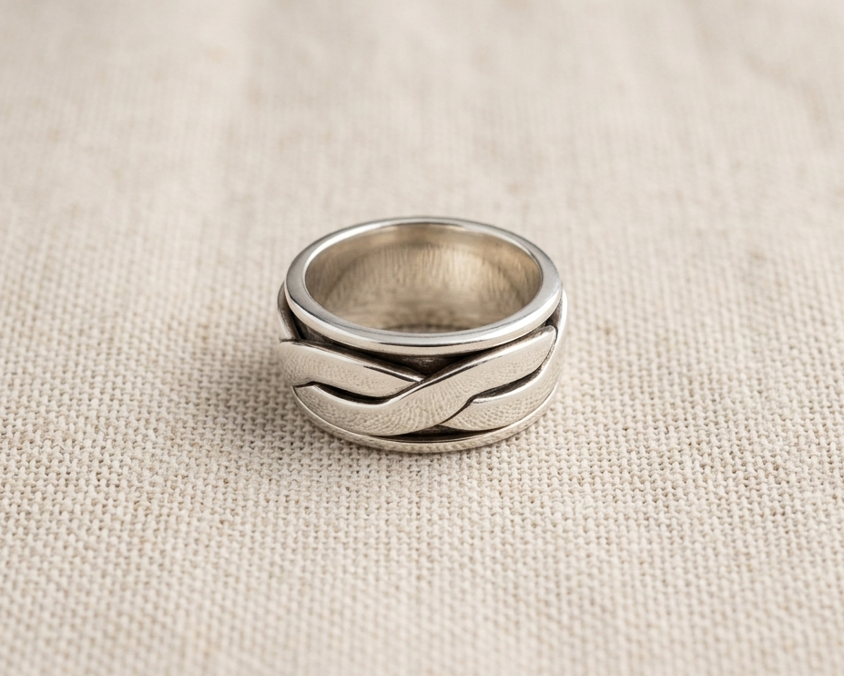 A detailed view of a high-polished sterling silver spinner ring, featuring an intricate woven-pattern inner band that rotates.