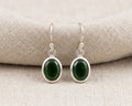 A pair of genuine dark green faceted oval jade drop earrings in polished .925 sterling silver bezel settings.