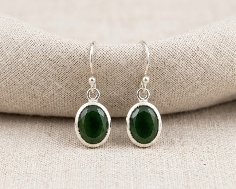 A pair of genuine dark green faceted oval jade drop earrings in polished .925 sterling silver bezel settings.