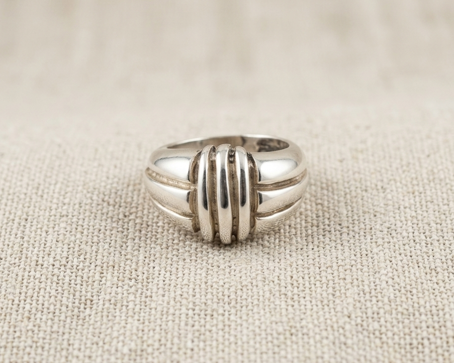 Substantial sterling silver statement ring with a domed, ribbed geometric design and high-polished finish, centered on a light-colored linen fabric background.
