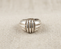 Substantial sterling silver statement ring with a domed, ribbed geometric design and high-polished finish, centered on a light-colored linen fabric background.