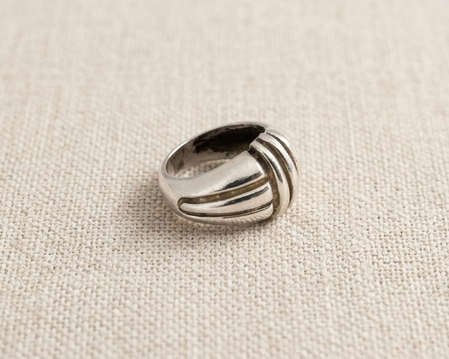 Substantial sterling silver statement ring with a domed, ribbed geometric design and high-polished finish, centered on a light-colored linen fabric background. Side view.
