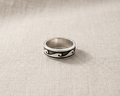 Sterling silver ring with deep-etched black enamel wave pattern band, displayed on a textured linen background with professional studio lighting.