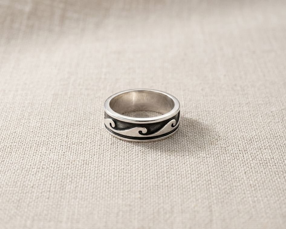 Sterling silver ring with deep-etched black enamel wave pattern band, displayed on a textured linen background with professional studio lighting.